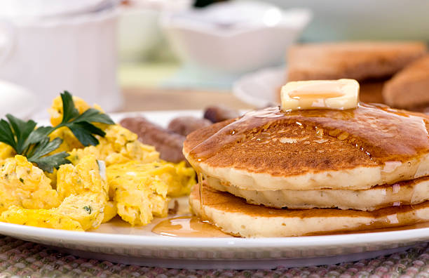A hearty breakfast plate with pancakes, eggs and sausages.